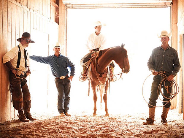 cowboys posing in stable with horse