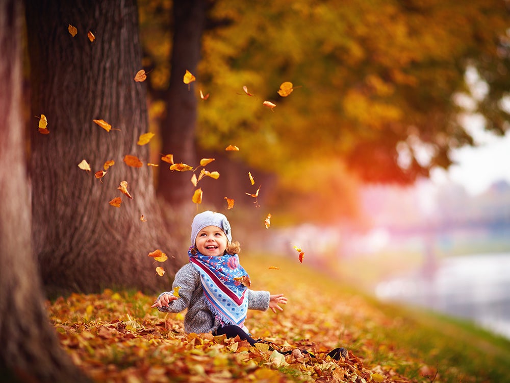 Adorable happy baby girl throwing the fallen leaves up, playing in the autumn park