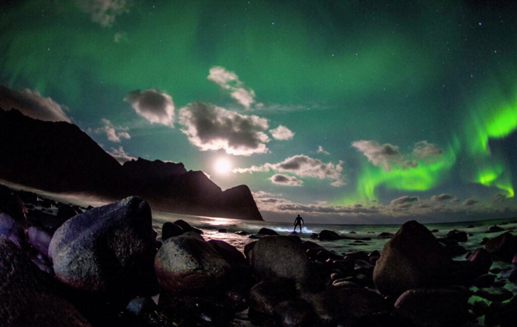 surfer beneath the northern lights green sky
