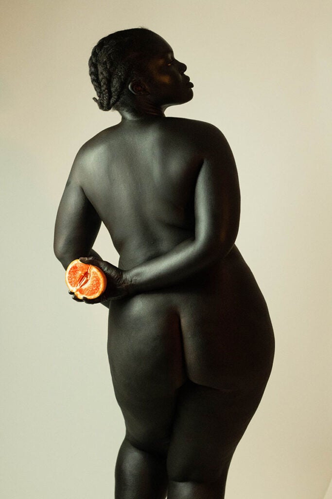 dark skinned woman holding fruit behind her back