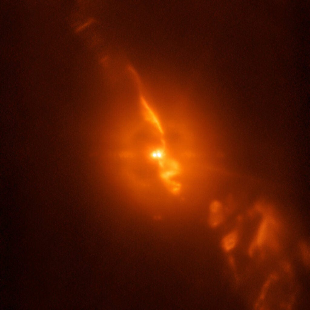 Two bright orange stars sit in a swirl of orange clouds made up of stellar material.