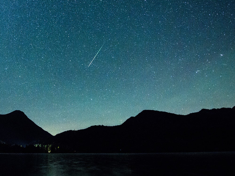 A shooting star appears next to the Milky Way in the sky above Walchensee.