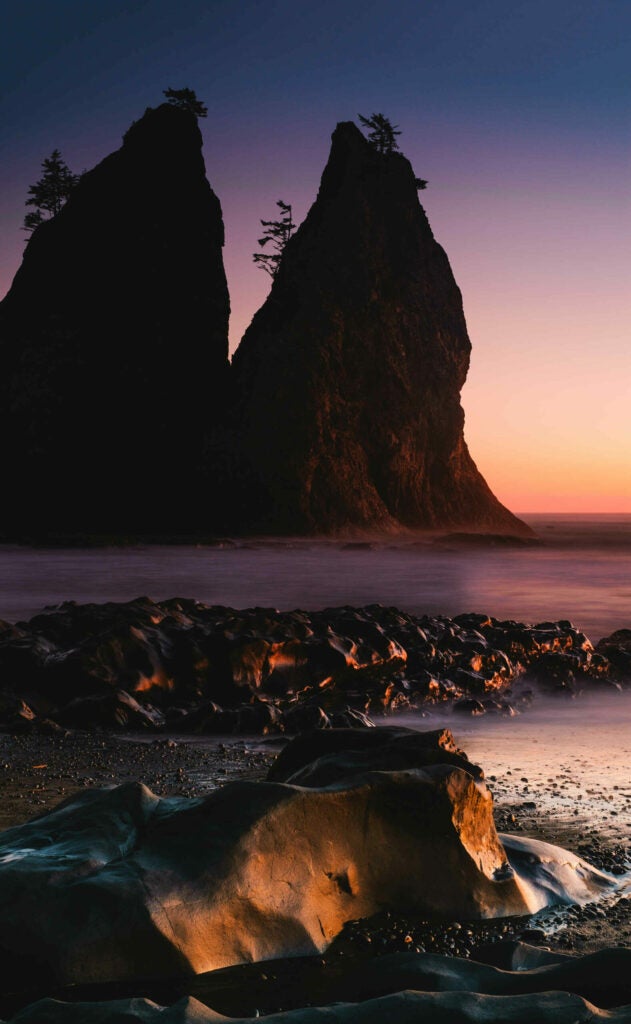 Seastacks silhouette the colorful sky, while carved rocks catch the last light of the day in the foreground, a bit after sunset on Rialto Beach in the Olympic Peninsula.