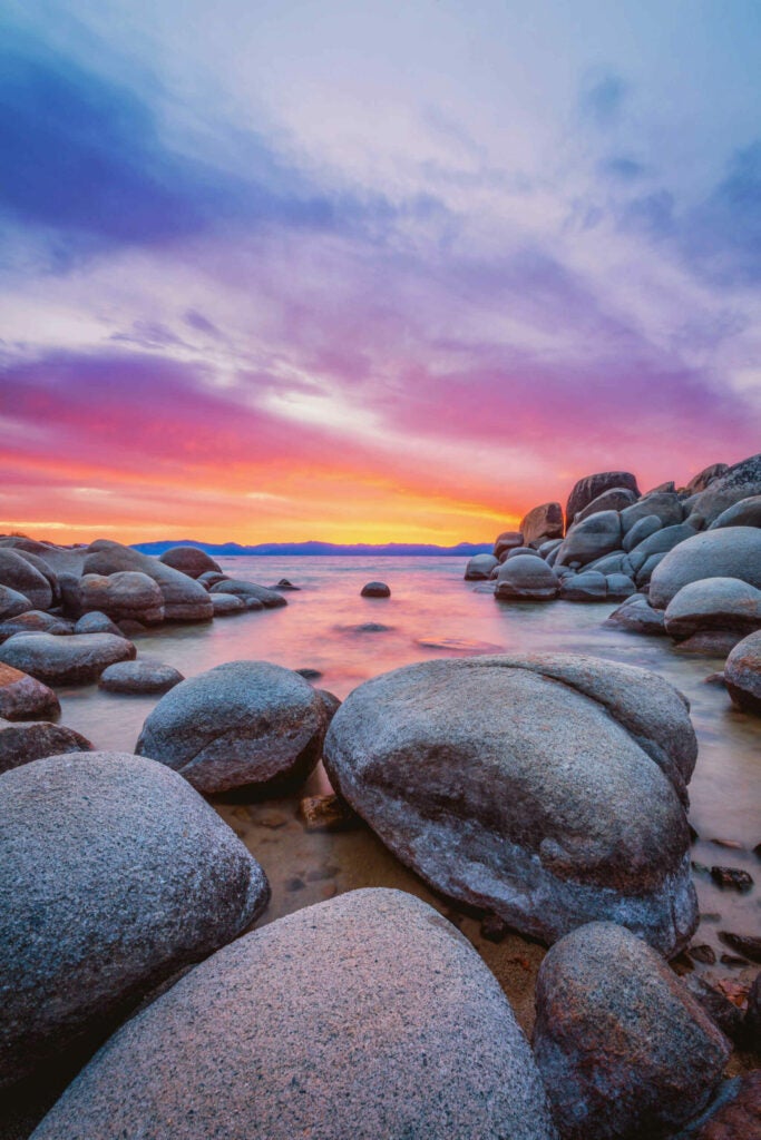 Sunset over Lake Tahoe on Sand Harbor Beach. One of the most beautiful sunsets I have seen. I just a wide angle lens to capture the size of the rocks. The sky looks like someone painted it with a brush. 
Shot with a nikon D800 and a NIkkor 16-35mm lens. I used a 3 stop grad ND. Processed in Lightroom, Edited for the final look in Photoshop.