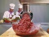 Minced meat coming through mincer with chefs in background