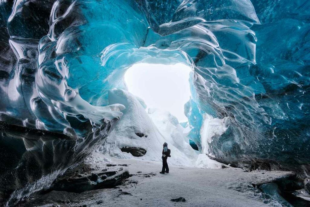 One Of The Most Amazing Places I Visited In Iceland Was This Ice Cave In The Vatnajökull Glacier National Park. This Park Is Home To One Of The Largest Ice Caps In Europe And The Largest In Iceland, Covering About 8% Of The Country. The Amazing Blue Color Of The Ice Is Created By The Increased Density Of The Glacial Ice. The Oxygen And Hydrogen Rich Ice Absorbs Most Of The Visible Color, But Reflects Back The Blues That You See In Here. This Is Quite A Stunning And Awe Inspiring Sight. My First Attempt At Capturing A Photo Of The Cave Was Without Anyone In The Frame, But I Quickly Realized That There Was A Complete Lack Of Scale. As I Was The Only One Standing Around I Needed To Figure Out How To Get Myself Into The Photo To Show Just How Big This Cave Really Was. I Also Had To Compensate For The Harsh Lighting Coming Through The Entrance Of The Cave. I Set My Camera For A 5 Exposure Bracket, Focused On A Point On The Ground Around Where I Would Stand And Set The Timer. I Then Quickly Ran Into Place And Stood Still While My Camera Took The 5 Shots.