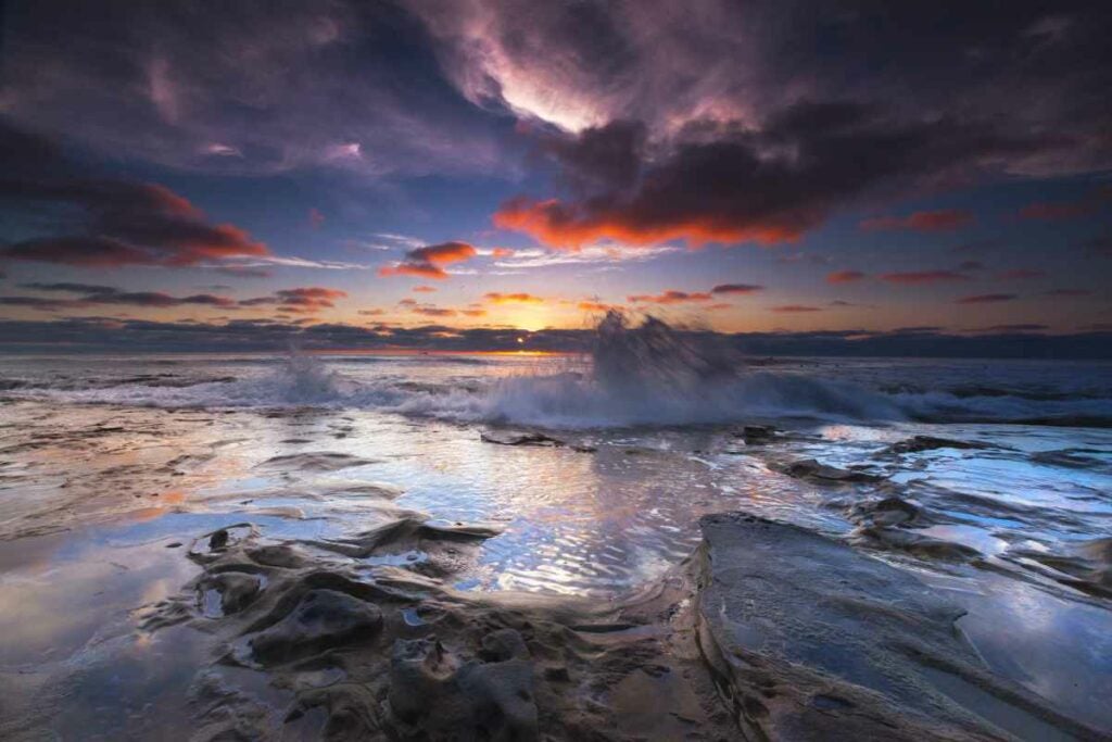 Sunset over La Jolla's Hospitals Reef while a wave reaches up to touch the clouds.