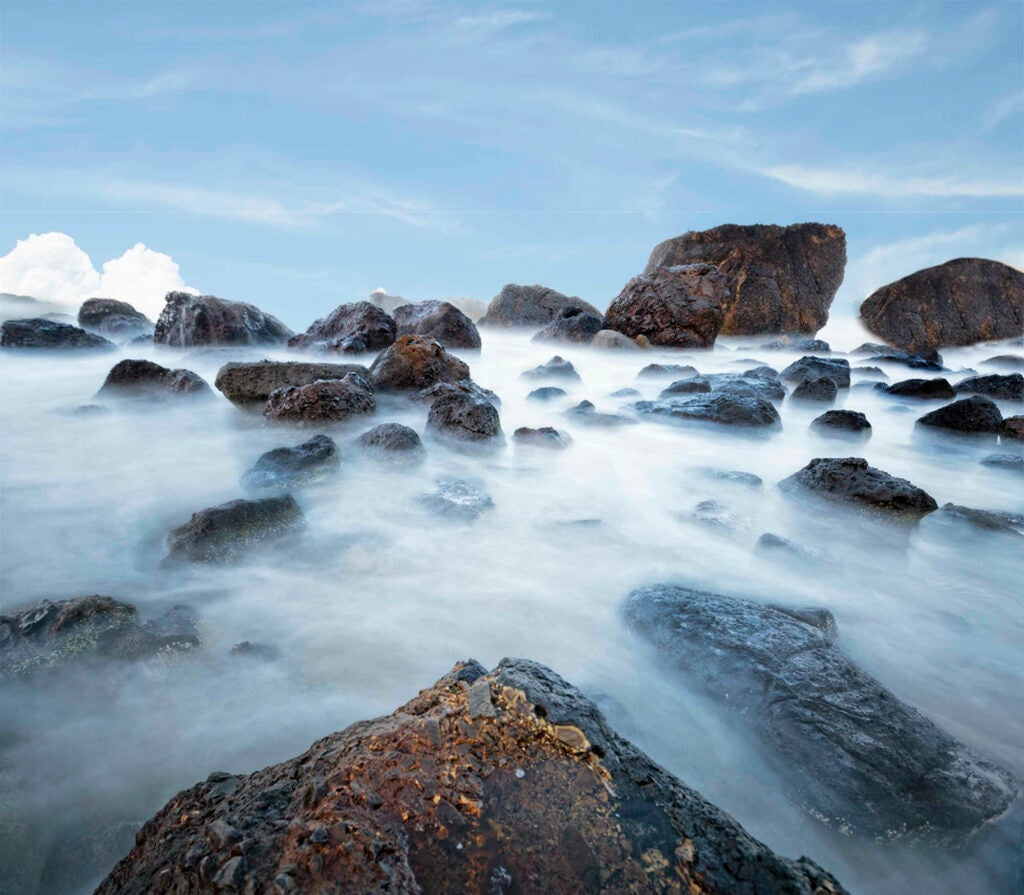 Indian Beach is near Cannon Beach in Oregon. It’s fabulous for photographers because of the “garden” of boulders at the water’s edge—plenty of perches for tripods to catch some long exposures. As long as you’re careful that while looking through your viewfinder, you’re not about to take a swim with your expensive equipment….I was lucky enough to have a sturdy friend with me that could keep me steady on my perch and at the same time keep an eye on the incoming waves. My equipment was a Canon 5D Mark III, Canon EF 16-35mm f/2.8L II USM Ultra Wide Angle Zoom Lens, a Vu 10-stop ND filter, and Manfrotto Pro 055XPROB Tripod Outfit with 804RC2 Pan Tilt Head. Other than some tweaking in Adobe Camera RAW and Photoshop CS6, there was little editing to the original picture of the water and rocks landscape. However, because of the ‘silky’ nature of the water after the long exposure, the water and overcast sky seemed to merge – couldn’t tell where one ended and the other began. So I imported a different sky, a blue one to give some separation. Is that cheating? Don’t know but it sure looked better. Settings were f4.5, ISO 100, for 30 seconds at 16mm.