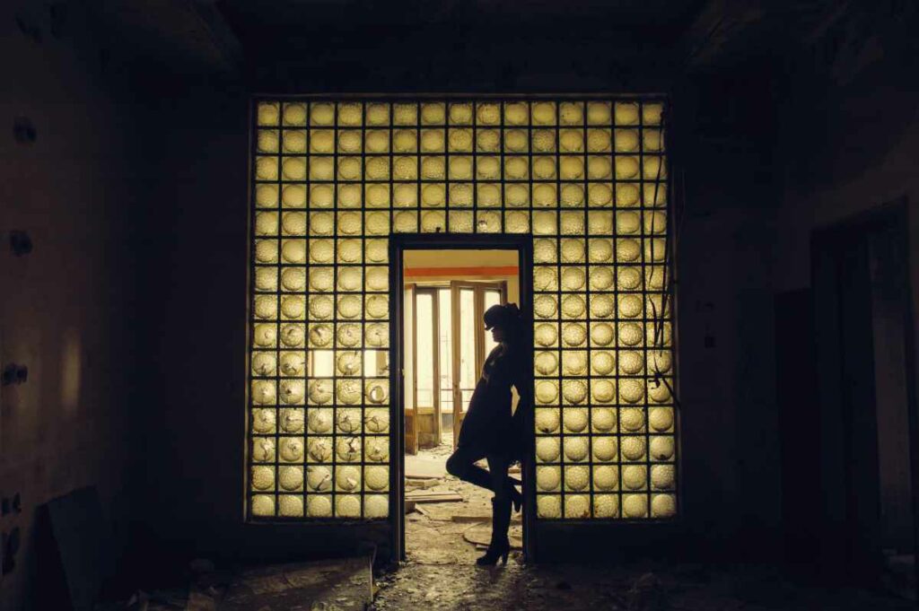 The silhouette of a young woman fills the frame of a door in an abandoned building.