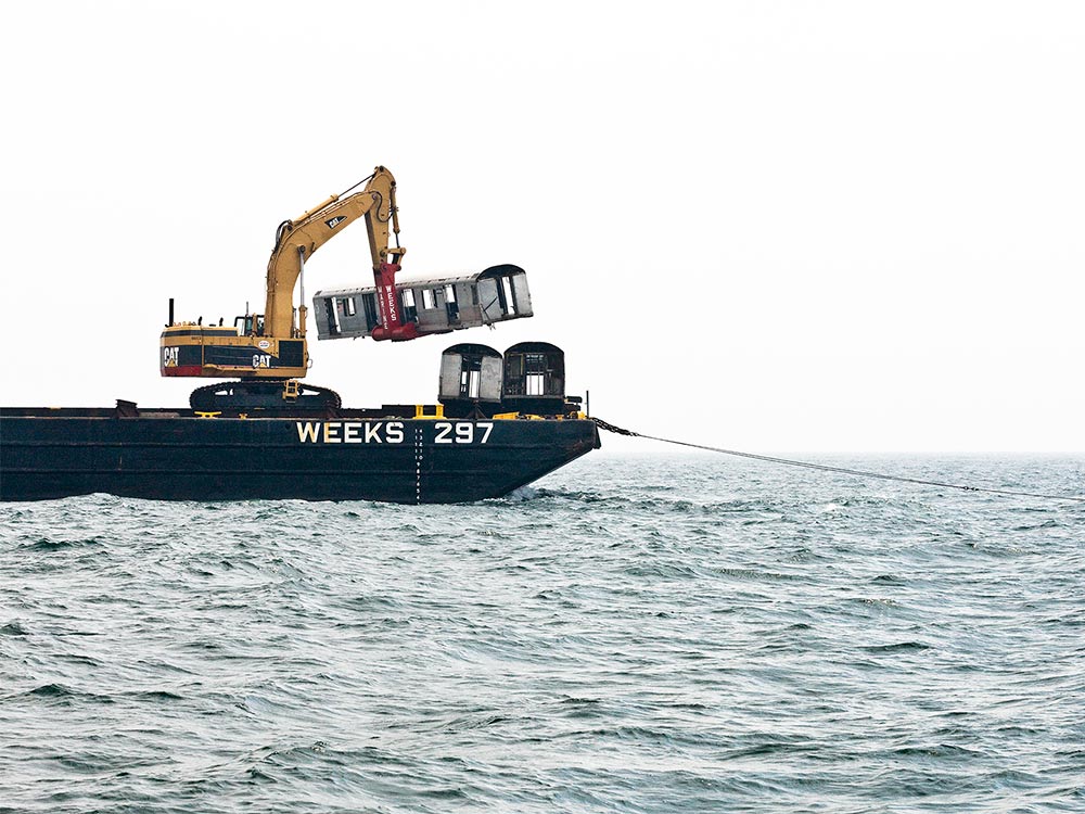 crane on week 297 lowering subway train cars into the ocean