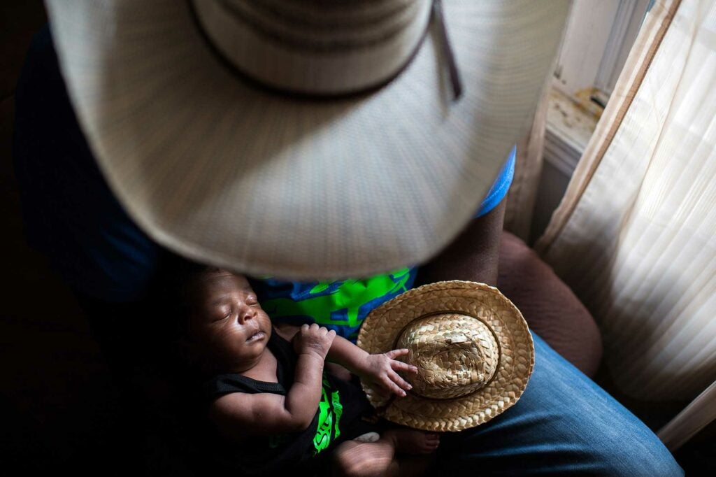 a baby in a man's lap holding a tiny cowboy hat