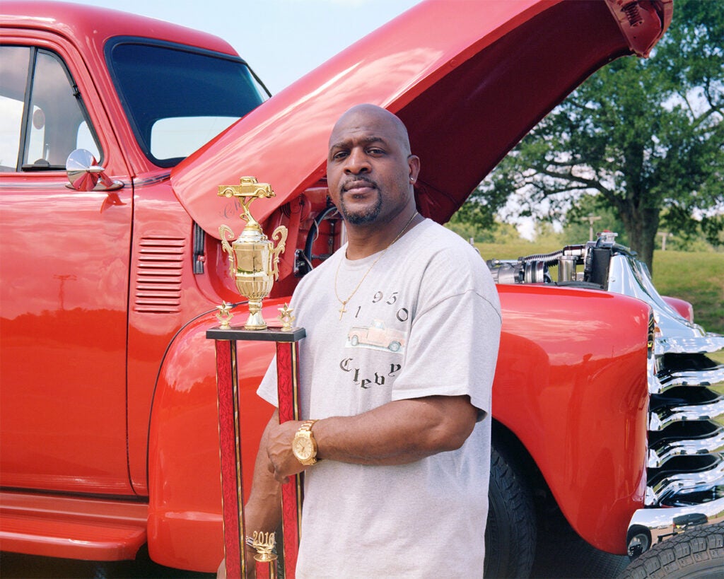 man with a trophy beside red vintage truck