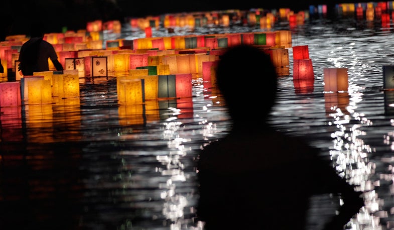 A man watches paper lanterns for the repose of the souls of the atomic bombing victims in the Motoyasu River near the Atomic Bomb Dome in Hiroshima, western Japan, Tuesday, Aug. 6, 2013. Japan marked the 68th anniversary Tuesday of the atomic bombing of Hiroshima with a somber ceremony to honor the dead and pledges to seek to eliminate nuclear weapons. (AP Photo/Shizuo Kambayashi)