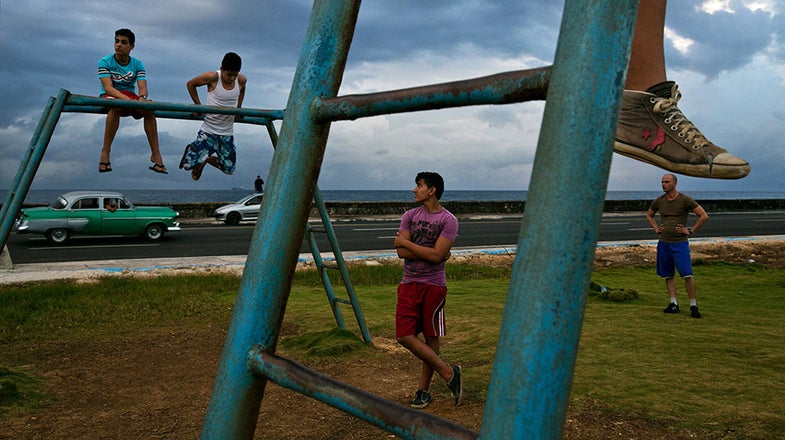 HAVANA, CUBA-Young Cuban men work out in a park along the Malecon as new and old cars drive past. New cars have become available in Cuba, but will be unattainable for most.