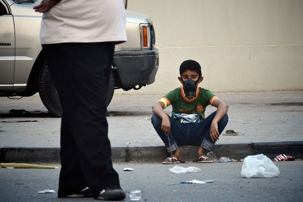 A Bahraini Shiite Muslim boy sits on the sidewalk wearing a gas mask during clashes with riot police after a demonstration in the village of Belad al-Qadeem in Bahrain.