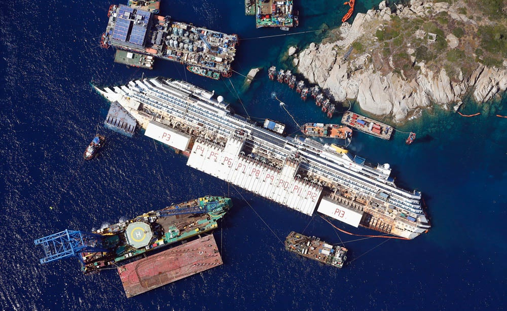 An aerial view shows the Costa Concordia as it lies on its side next to Giglio Island taken from an Italian navy helicopter August 26, 2013. The wrecked Costa Concordia cruise ship could be upright again next week, nearly two years after the liner capsized and killed at least 30 people off the Italian coast. The giant vessel, which has lain partly submerged in shallow waters off the Tuscan island of Giglio since the accident in January 2012, will be rolled off the seabed and onto underwater platforms.  Picture taken August 26, 2013.   (ITALY - Tags: MARITIME DISASTER TRANSPORT) - RTX13IP0