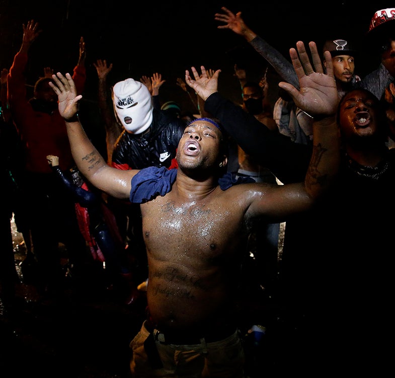 People defy a curfew Sunday, Aug. 17, 2014, before smoke and tear gas was fired to disperse a crowd protesting the shooting of teenager Michael Brown last Saturday in Ferguson, Mo. Brown's shooting in the middle of a street following a suspected robbery of a box of cigars from a nearby market has sparked a week of protests, riots and looting in the St. Louis suburb. (AP Photo/Charlie Riedel)