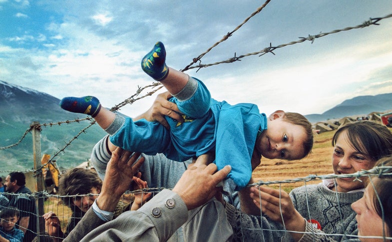 2000 Feature Photography Pulitzer Prize REUNION May 3, 1999 Kosovar refugee Agim Shala, 2 years old, is passed through the barbed wire fence into the hands of grandparents at the camp run by United Arab Emirates in Kukes, Albania. The members of the large Shala family were reunited here after fleeing Prizren in Kosovo during the conflict. . (The grandparents had just crossed the border at Morina). The relatives who just arrived had to stay outside the camp until shelter was available. The next day members of the family had tents inside. The fence was the scene of many reunions. When the peace agreement was signed, they returned to Prizren to find their homes only mildly damaged. There were tears of joy and sadness from the family as the children were passed through the fence, symbolic of the innocence and horror of the conflict.