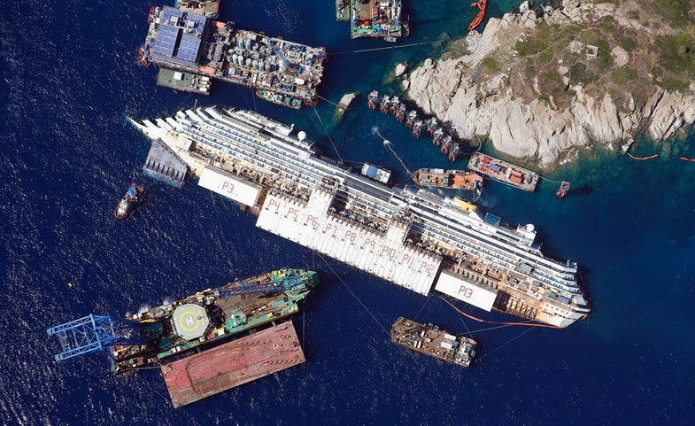 An aerial view shows the Costa Concordia as it lies on its side next to Giglio Island taken from an Italian navy helicopter August 26, 2013. The wrecked Costa Concordia cruise ship could be upright again next week, nearly two years after the liner capsized and killed at least 30 people off the Italian coast. The giant vessel, which has lain partly submerged in shallow waters off the Tuscan island of Giglio since the accident in January 2012, will be rolled off the seabed and onto underwater platforms. Picture taken August 26, 2013. (ITALY - Tags: MARITIME DISASTER TRANSPORT) - RTX13IP0