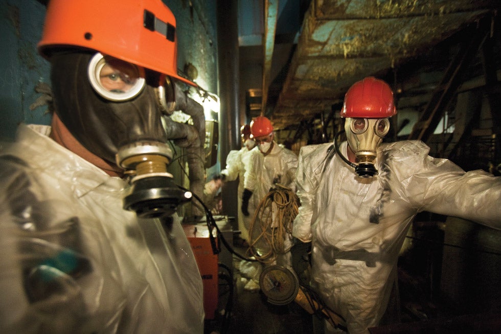 Workers wearing plastic suits and respirators for protection pause briefly on their way to drill holes for support rods inside the shaky concrete sarcophagus, a structure hastily built after the explosion to isolate the radioactive rubble of Reactor #4. Their job is to keep the deteriorating enclosure standing until a planned replacement can be built.  It is hazardous work: radiation inside is so high that they constantly need to monitor their Geiger counters – and are allowed to work only one shift of 15 minutes per day. The Long Shadow of Chernobyl - Photographs © Gerd Ludwig/INSTITUTE