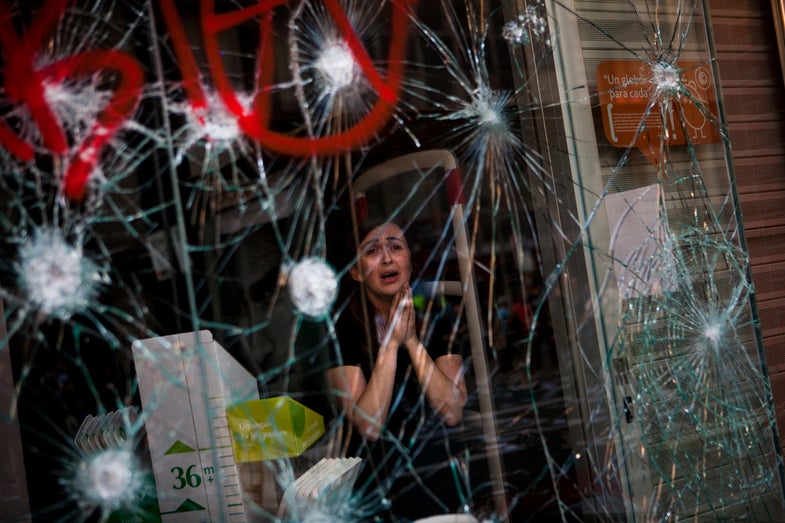 Mirian Burrueco, 30, reacts behind the broken glass of her shop stormed by demonstrators during clashes at the general strike in Barcelona, Thursday, March 29, 2012. Spanish workers livid over labor reforms they see as flagrantly pro-business staged a nationwide strike Thursday and tried to bring the country to a halt by blocking traffic, closing factories and clashing with police in rowdy demonstrations. (AP Photo/Emilio Morenatti)