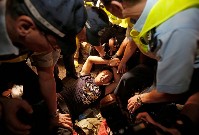 A man is cuffed by police and taken from the confrontation of pro-democracy student protesters and angry local residents in Mong Kok, Hong Kong, Friday, Oct. 3, 2014. Pushing and yelling, hundreds of Hong Kong residents tried to force pro-democracy activists from the streets they were occupying Friday as tensions rose in the weeklong protests that have shut down parts of the city. (AP Photo/Wally Santana)