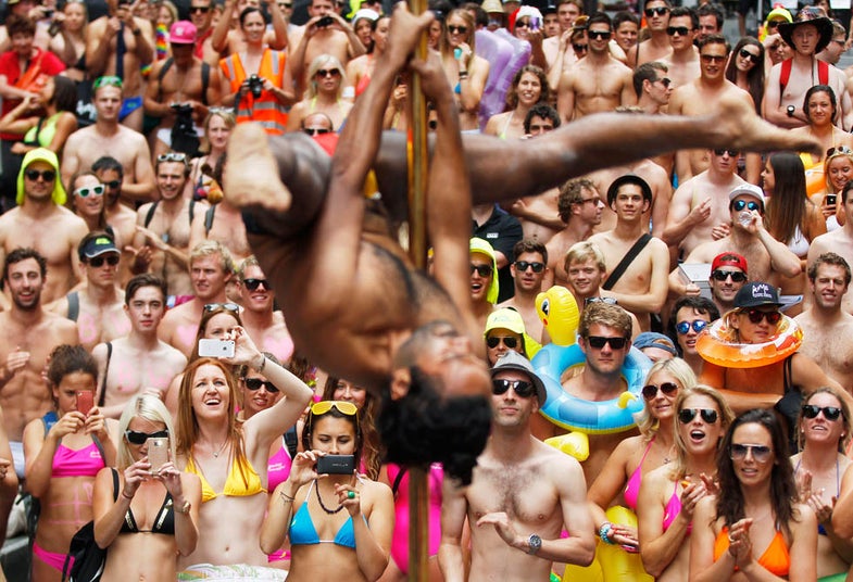 Participants of 'Strut the Streets', an annual swimwear parade, look at a man pole dancing in central Sydney December 7, 2012. 'Strut the Streets' raises money to help aboriginal Australians to finish school at the same rate as every Australian child. REUTERS/Daniel Munoz (AUSTRALIA - Tags: SOCIETY TPX IMAGES OF THE DAY)