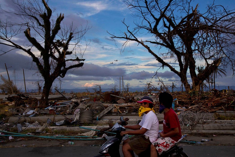 Typhoon Haiyan survivors pass by on a scooter as two U.S. Osprey aircraft fly over the ruins of Tacloban, central Philippines on Wednesday, Nov. 13, 2013. Typhoon Haiyan, one of the most powerful storms on record, hit the country's eastern seaboard on Friday, destroying tens of thousands of buildings and displacing hundreds of thousands of people. (AP Photo/David Guttenfelder)