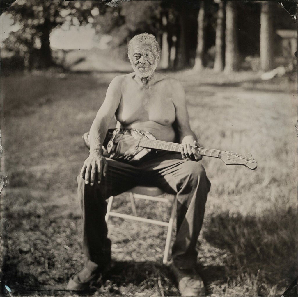 Freeman Vines shirtless with instrument in a field