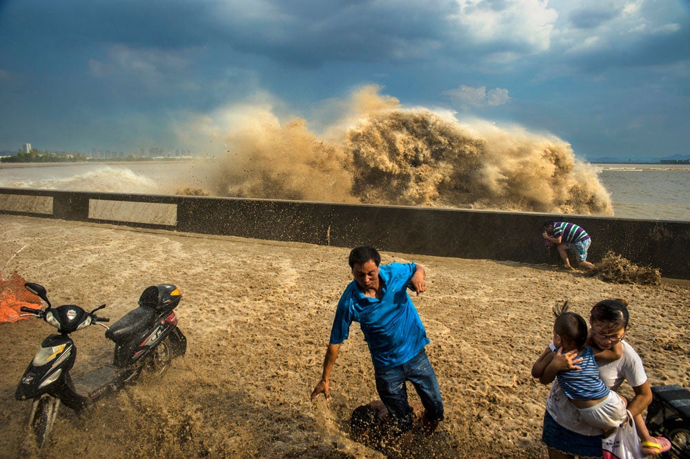 Visitors run away as waves from a tidal bore surge past a barrier on the banks of Qiantang River, in Hangzhou Zhejiang province, August 24, 2013. Picture taken August 24, 2013. REUTERS/Stringer (CHINA - Tags: ENVIRONMENT TPX IMAGES OF THE DAY) CHINA OUT. NO COMMERCIAL OR EDITORIAL SALES IN CHINA - RTX12VNG
