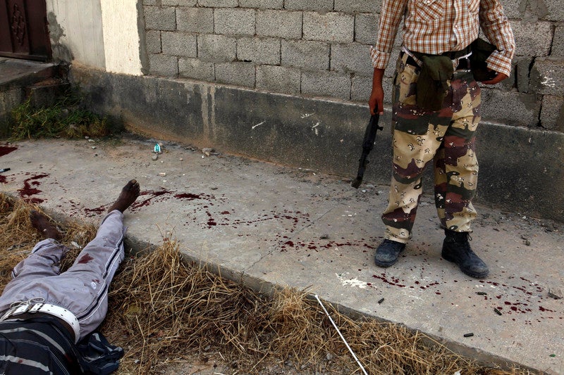 A rebel stands over the dead body of an alleged mercenary, killed during fighting in Tripoli, Libya, Aug. 25, 2011.