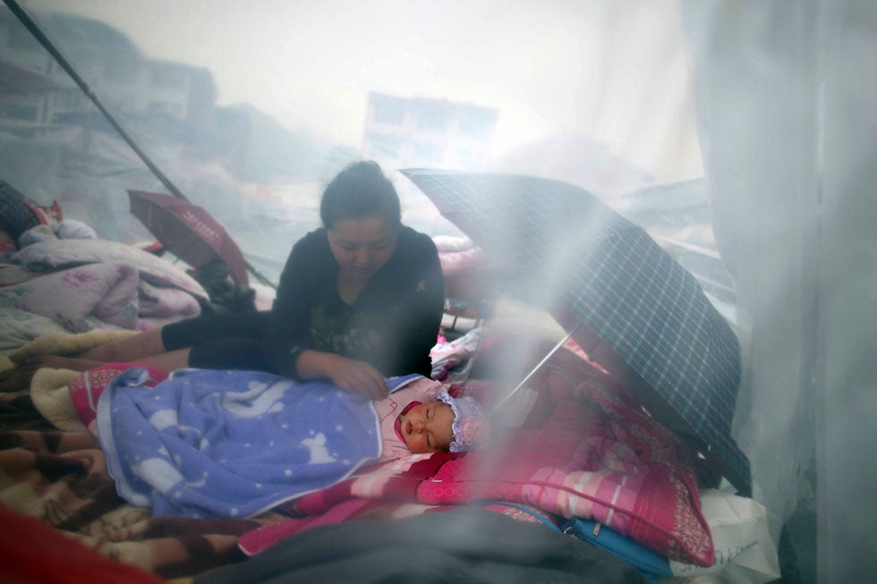 A woman and her child rest among wreckage of Saturday's earthquake in Lingguan, China. Rescuers struggled to reach a remote, rural corner of southwestern China on Sunday as the death toll climbs to 186 people dead and 11,393 injured, Xinhua News Agency reported.