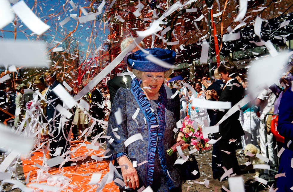 Queen Beatrix of the Netherlands is greeted by a cheering crowd and ticker tape in the city of Veenendaal , during a parade to celebrate the annual Queens' day holiday.