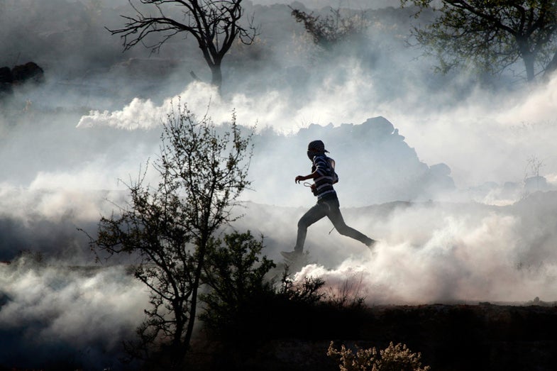 A Palestinian demonstrator runs through a cloud of tear gas during clashes against Israel's operations in Gaza Strip, outside Ofer, an Israeli military prison near the West Bank city of Ramallah, Thursday, Nov. 15, 2012. Meanwhile, Palestinian President Mahmoud Abbas cut short a trip to Europe to deal with the crisis. (AP Photo/Majdi Mohammed)