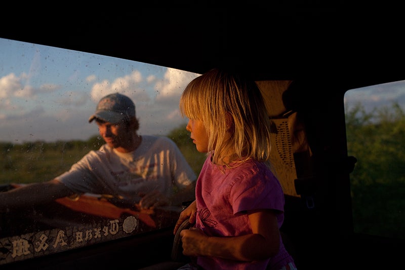 Mirabelle, 3, watches her father from inside the family farm pick-up truck. Fred Lyssy, left, does evening chores around the family's 564-acre organic farm. Fracking activity surrounding the Lyssy's farm in the Eagle Ford Shale has brought dangerous air emissions, including benzene and hydrogen sulfide, which cause great concern for the Lyssy family and their legacy farm. <em>Lance Rosenfield is a freelance photographer based in Washington, DC. Lance's project 'Thirst for Grit' was chosen as a finalist for the 2009 Emerging Photographer Grant awarded by the Magnum Foundation, as well as the Michael P. Smith Grant for Documentary Photography. See more of his work <a href="http://www.rosenfieldphotography.com/">here. </a></em>