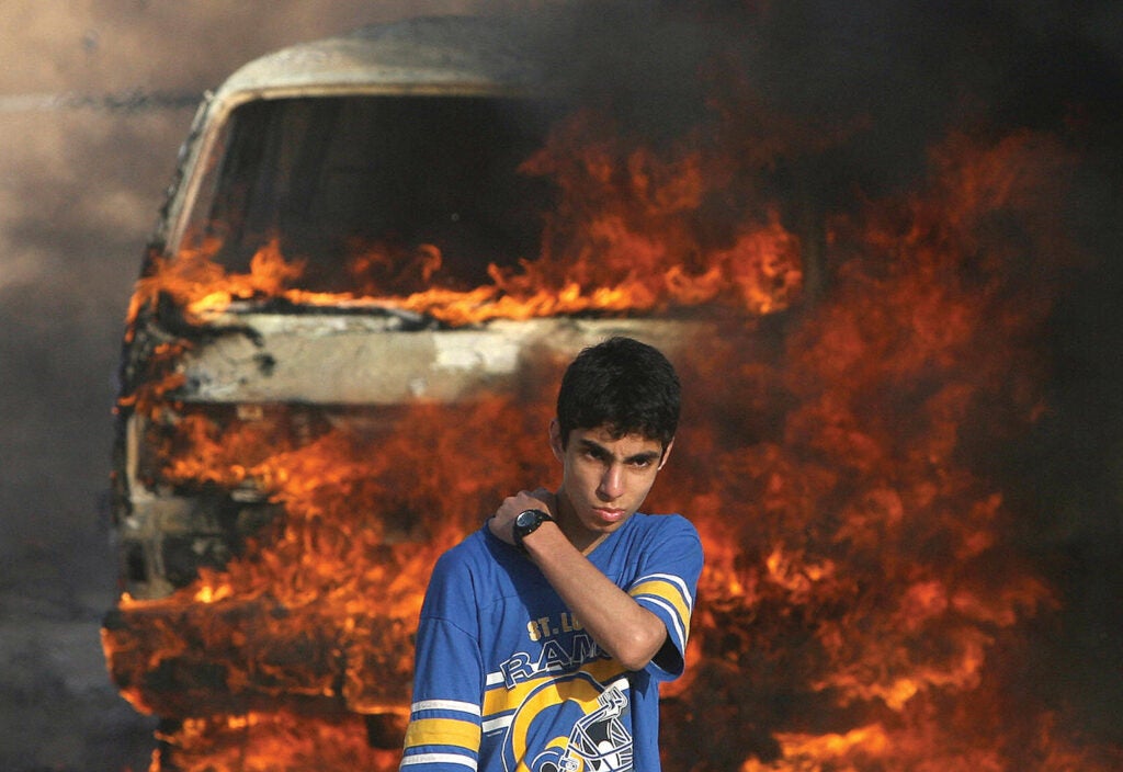 A Palestinian youth stands in front of a burning vehicle during clashes between rival Fatah and Hamas in Gaza City, May 14, 2007. From: <em>War is Beautiful</em> by David Shields, published by powerHouse Books.