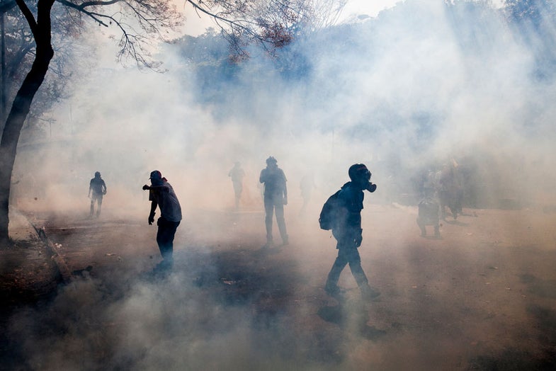 Demonstrators walk through a cloud of tear gas fired by the Bolivarian National Police during clashes in Caracas, Venezuela, Wednesday, March 12, 2014. According to local authorities, several deaths have been reported Wednesday, and a number of others, including National Guardsmen, have been wounded after being shot by unknown assailants in separate incidents in the central Venezuelan city of Valencia. (AP Photo/Alejandro Cegarra)