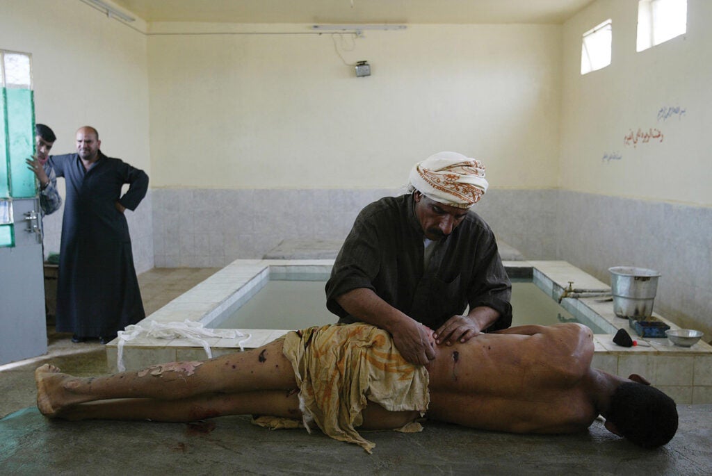 Ali Hadi, a professional body washer, prepares the body of a bombing victim for Muslim burial as the man's relatives watch in Najaf, Iraq. From: <em>War is Beautiful</em> by David Shields, published by powerHouse Books.