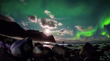 surfer beneath the northern lights green sky