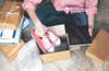 person surrounded by packages with ipad in hand putting shoes in box for shipment