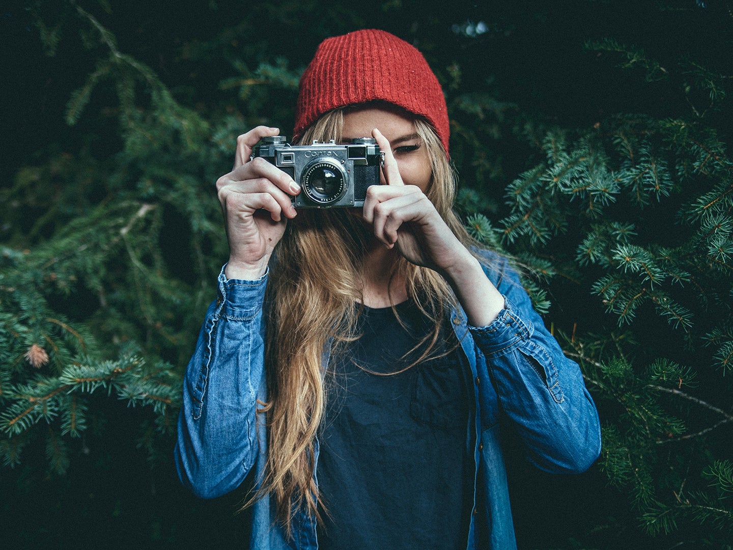 photographer in red hat against evergreen trees