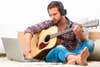 Person on sofa playing the guitar with laptop at home