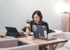 a woman at a wooden table using a Windows tablet or laptop next to another Windows laptop