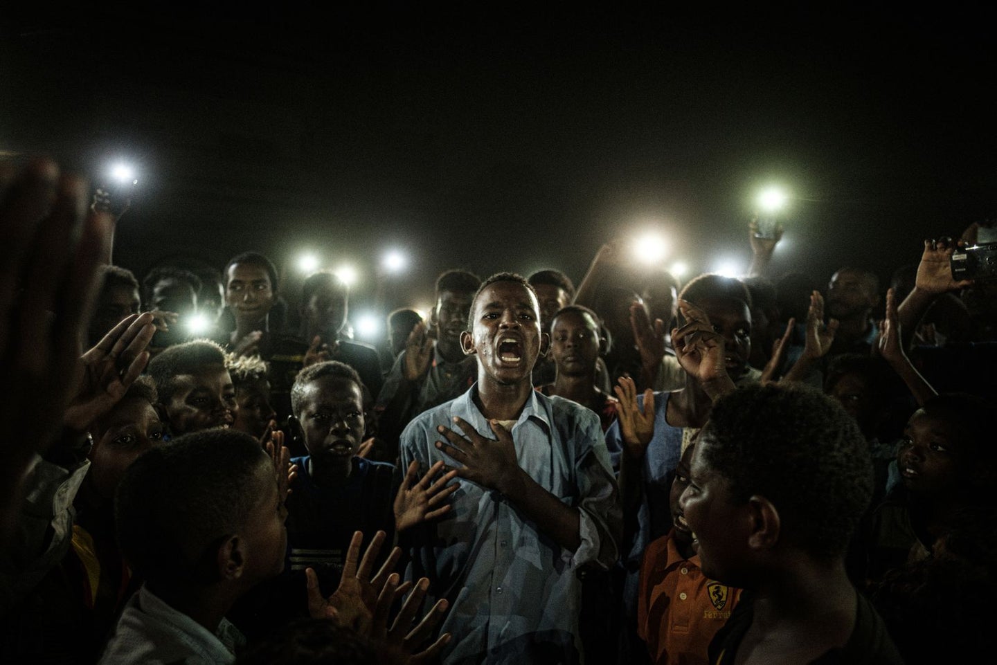 A young man, illuminated by mobile phones, recites protest poetry while demonstrators chant slogans calling for civilian rule, during a blackout in Khartoum, Sudan, on 19 June.