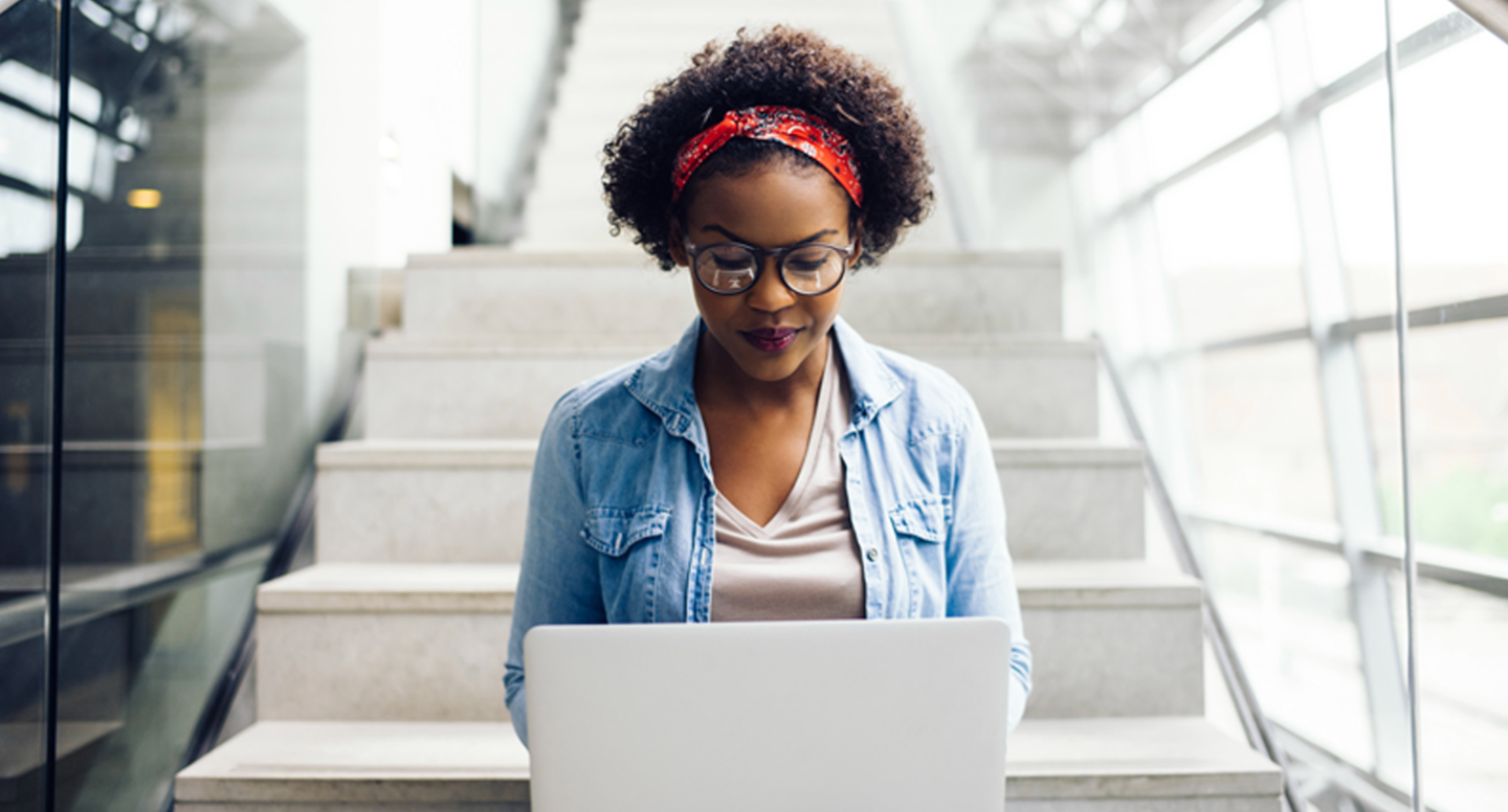 Woman sitting on the stairs using a white laptop