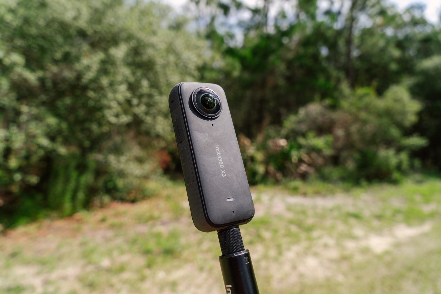 An Insta360 X3 on a selfie stick in the woods