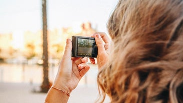 brunette woman holding a point-and-shoot camera outdoors