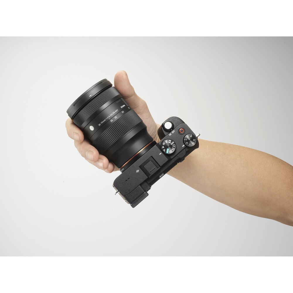A hand holding Sony's new 28-70mm zoom lens attached to a Sony mirrorless camera body.