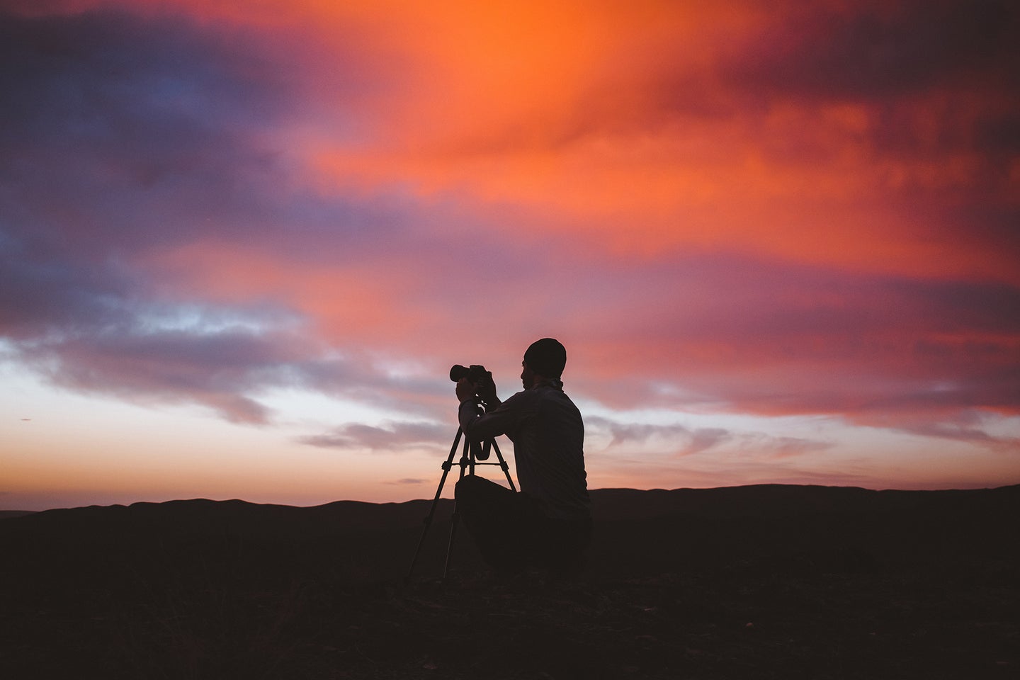 guy with a camera in a tripod with an organge and purple sky behind him