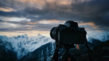 Best full frame camera on a tripod in front of a cloudy sky and snowy mountain